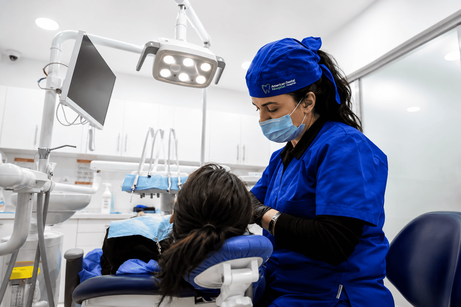 Dentista in camice blu e mascherina che cura un paziente in una clinica odontoiatrica.