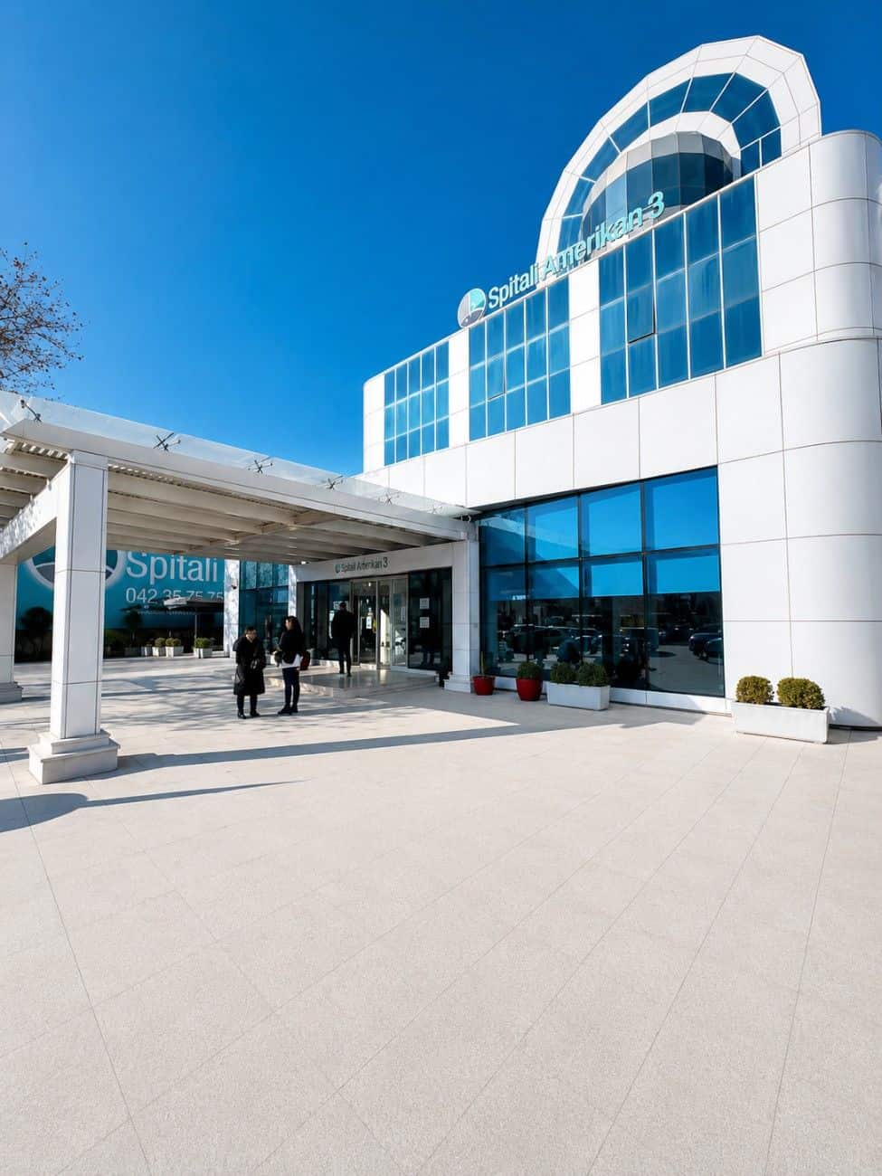Modern hospital building with blue glass windows and white exterior under clear sky.
