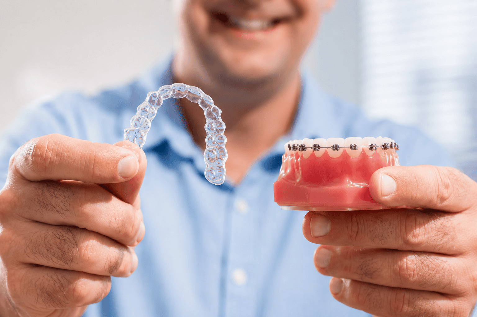 Dentist holding a clear aligner and a dental model with braces in a dental clinic.