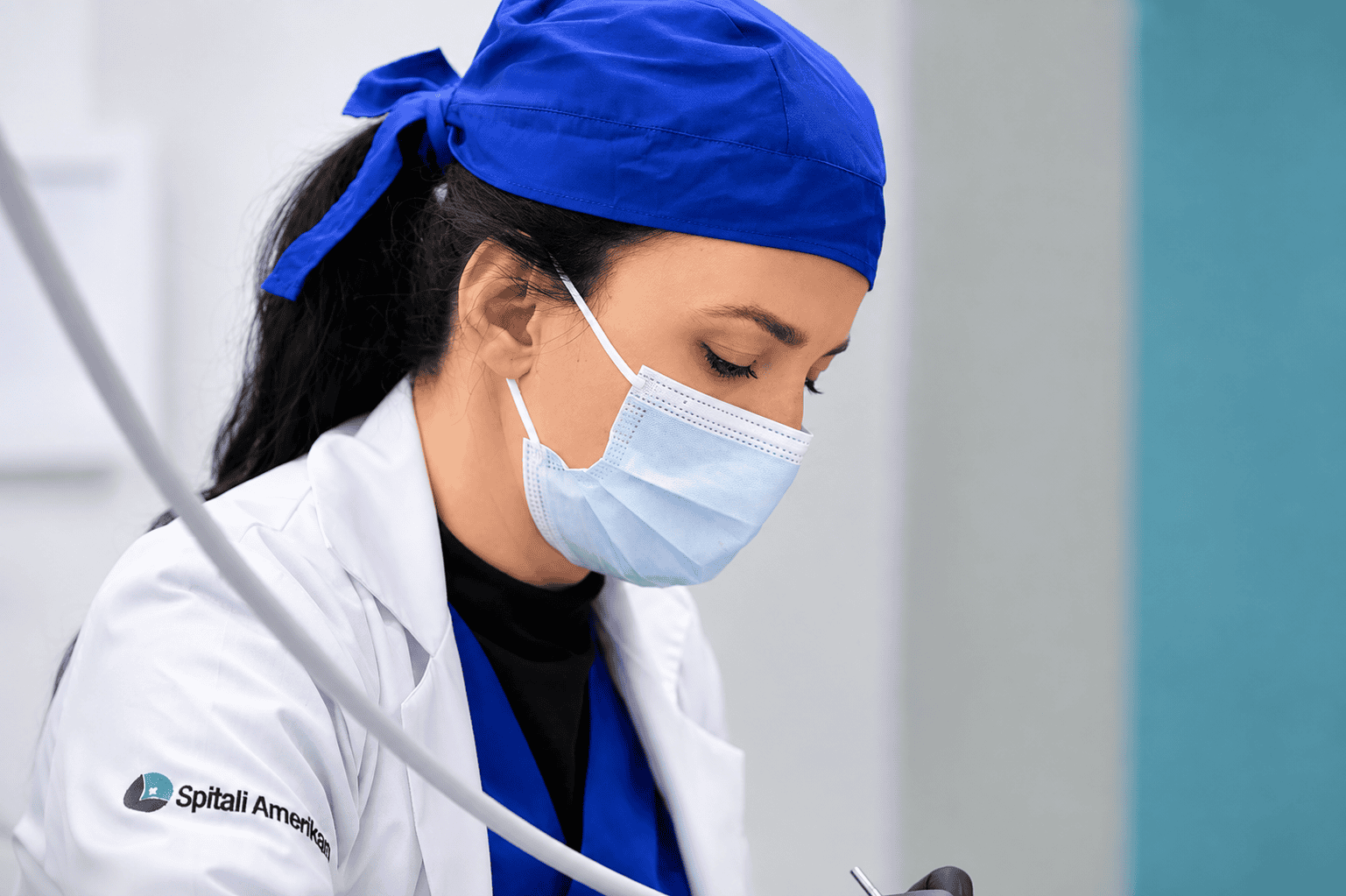 Female healthcare professional in scrubs and mask working in a medical setting.