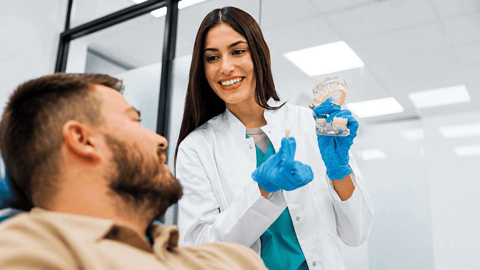 Dental professional showing dental model to patient in clinic.