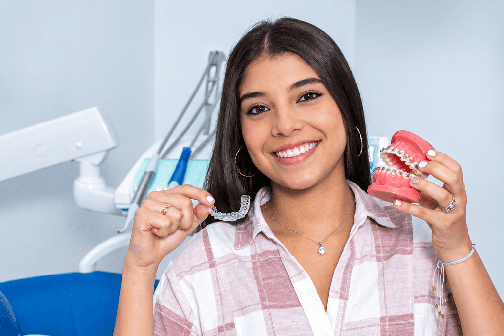 Smiling woman holding dental retainer and model teeth in dental clinic.