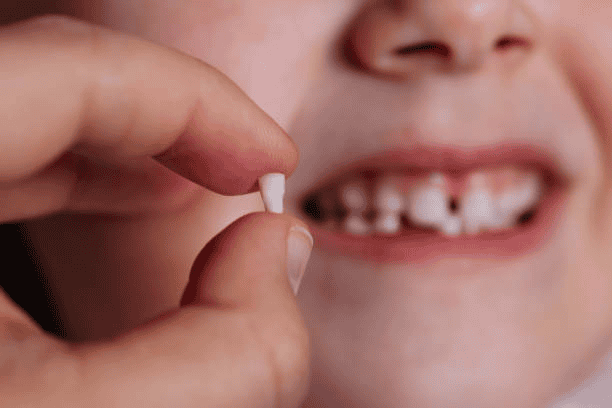 Child holding a small white pill near their mouth, smiling with missing teeth.