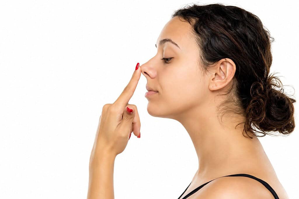 Woman touching her nose, considering rhinoplasty or nose surgery options.